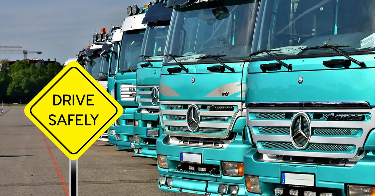 ‘Drive safely’ road sign in front of a row of commercial trucks